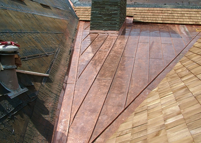 A complex roof structure featuring a combination of copper and wooden shingles, showcasing intricate craftsmanship.